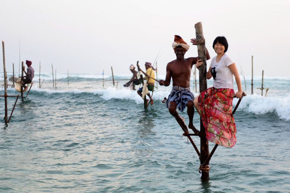 A Chinese tourist poses at a stilt fishing pole in Sri Lanka. Photo: Xinhua