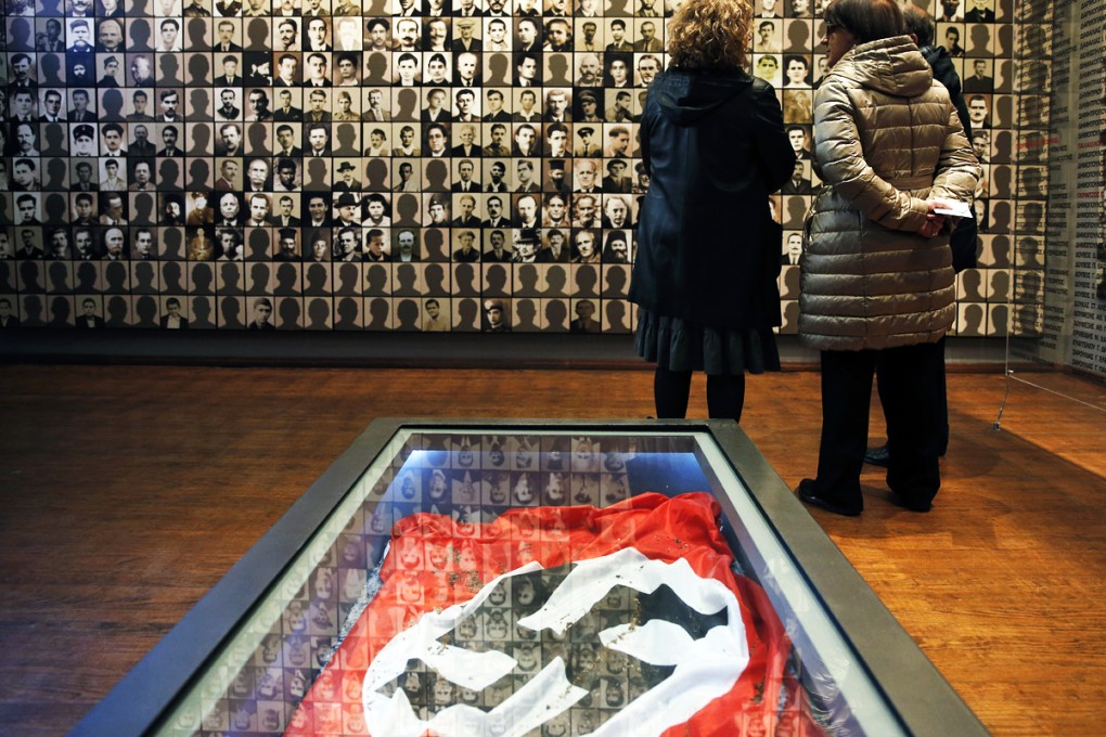 Visitors look at portraits of victims at the Holocaust Museum in the town of Kalavryta, western Greece, in front of a Nazi flag. Photo: AP