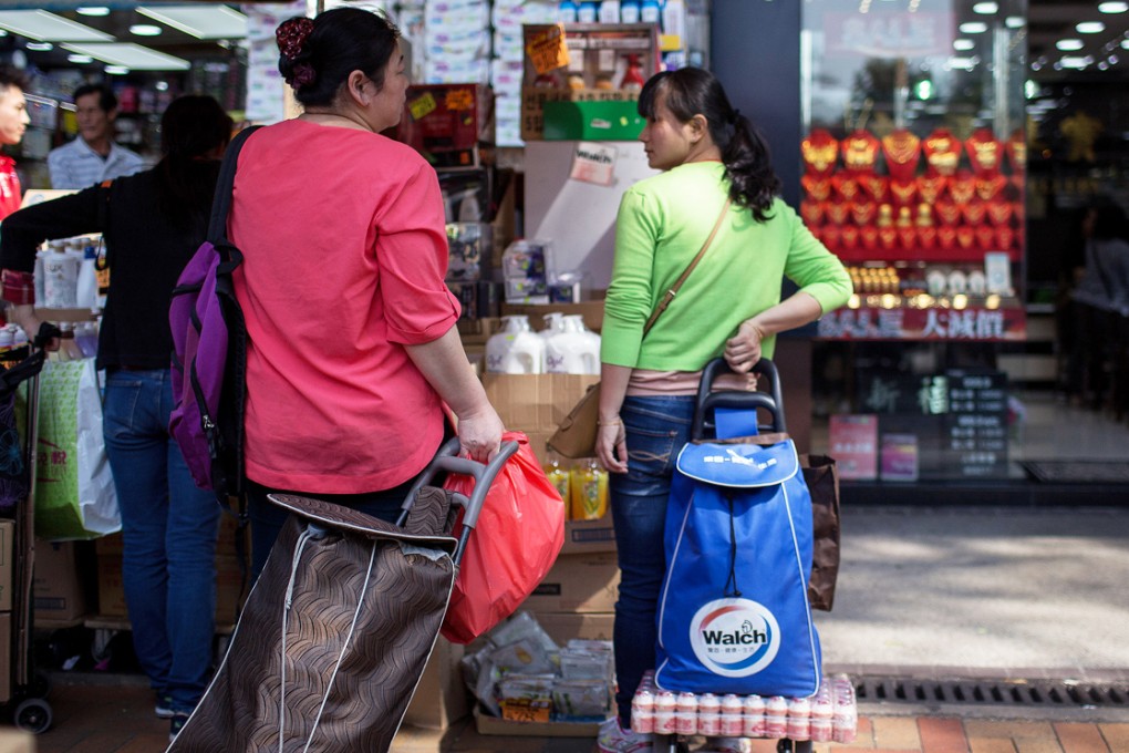 Shoppers hold shopping carts stand outside a pharmacy (left) and a jewelry store in the Sheung Shui  near the border with mainland China. Photo: Bloomberg