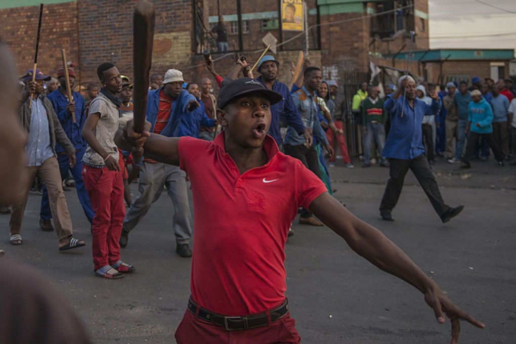 A man raises a baton to intimidate members of the media, as the mob threatens to burn down foreign shops and drive out their owners. Photo: AFP