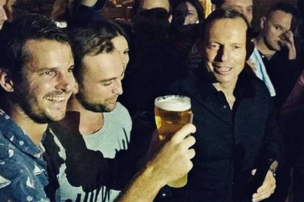 A still from the video shows Tony Abbott (right) accepting the invitation to sheer a celebratory beer with football players at a Sydney pub.