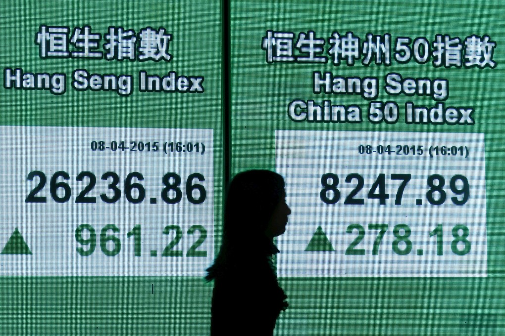Electronic screens showing stock indexes frame a woman in Hong Kong. Photo: Reuters