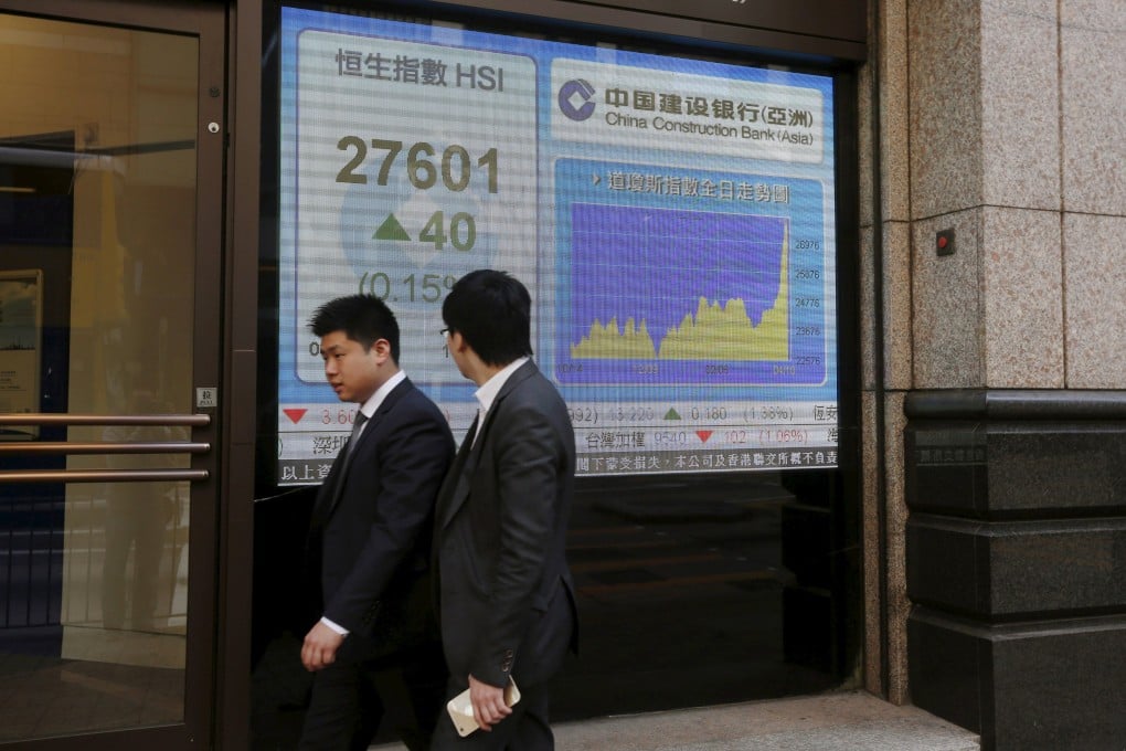 Businessmen walk past an electronic board showing the Hang Seng index which surged at the start on Monday to hit fresh highs along with the Shanghai index in China. Photo: Reuters