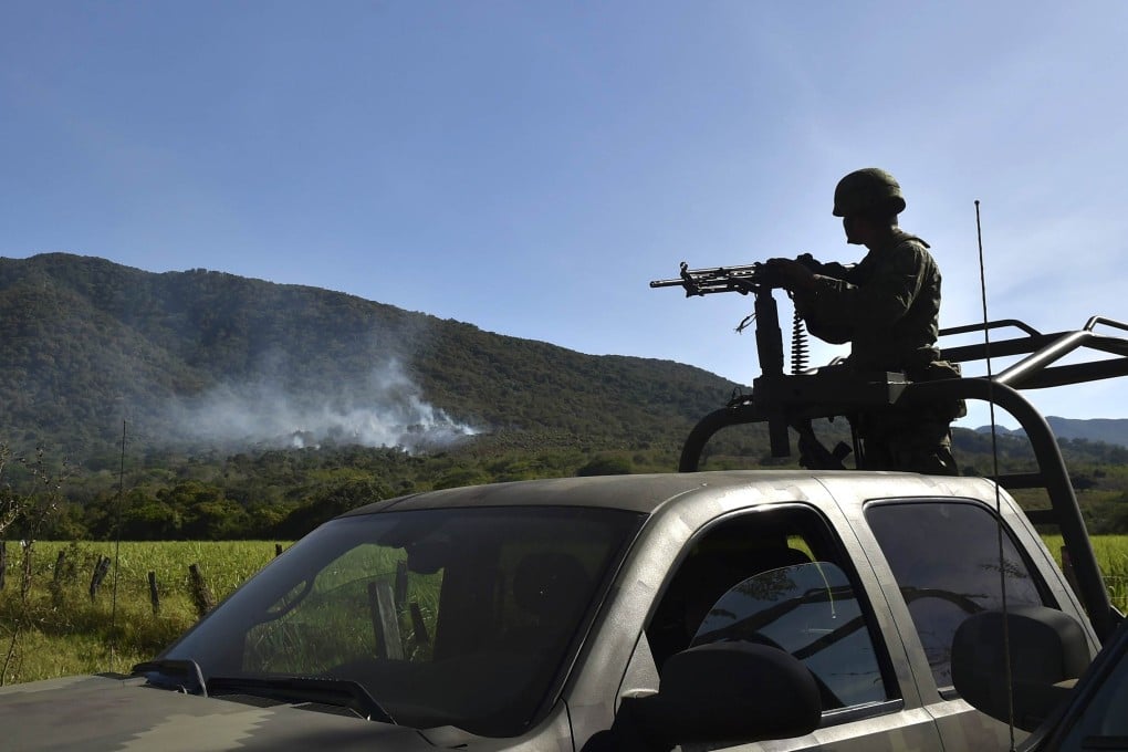 A Mexican soldier looks on as smoke rises from the scene where a military helicopter was shot down on Friday. Photo: AFP