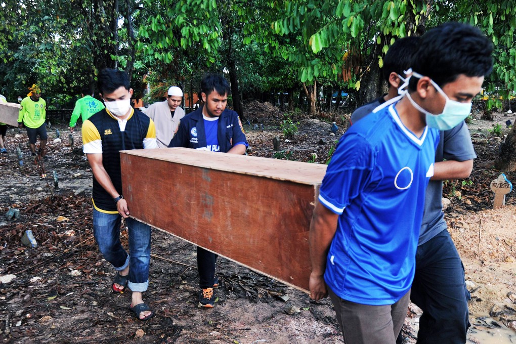 Rescue workers carry coffins containing the human remains of migrants exhumed at the weekend at an abandoned jungle camp in the Sadao district, Thailand. Photo: AFP