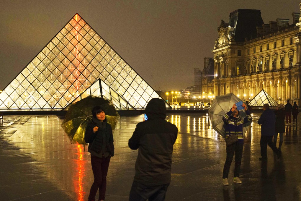Chinese tourists take photos of each other outside the main entrance to the Louvre museum and its pyramid in Paris. Photo: AFP