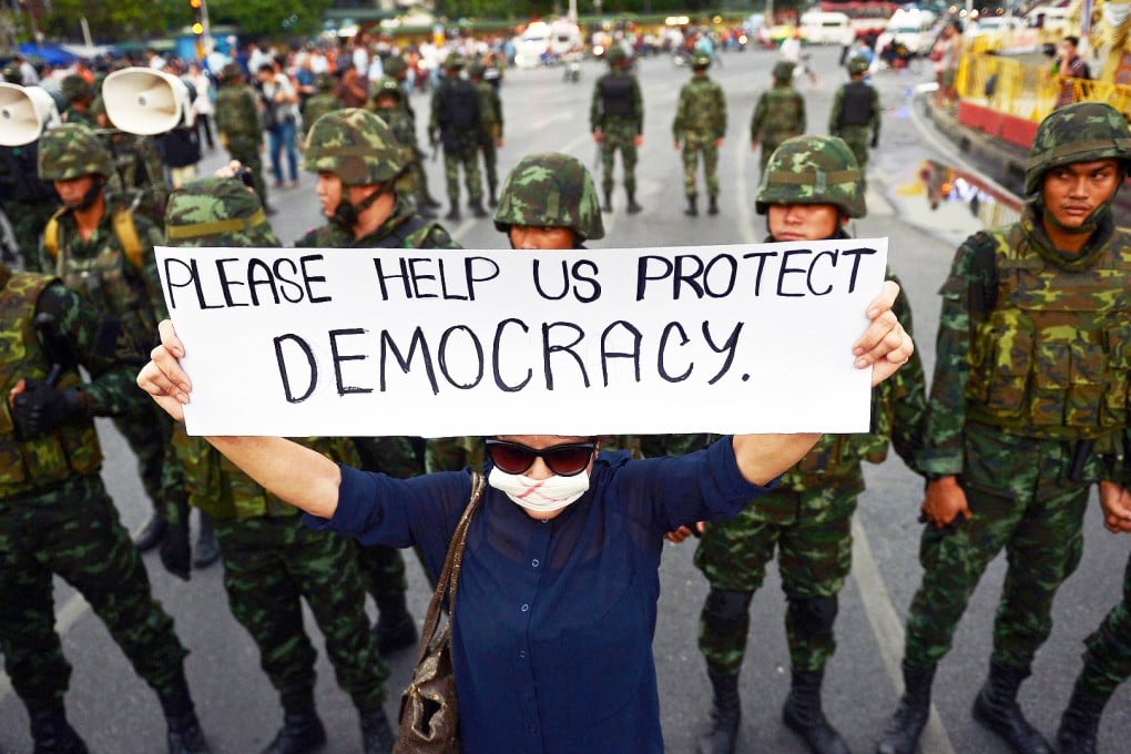 An anti-coup protester holds up a sign near soldiers as she takes part in a rally in Bangkok. On Friday, the anniversary of the coup, police quashed a small, peaceful demonstration in the city. Photo: AFP