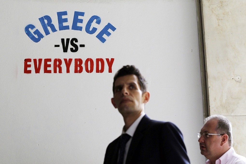 Pedestrians walk past stenciled graffiti on a wall outside a bank in Athens. Photo: AP