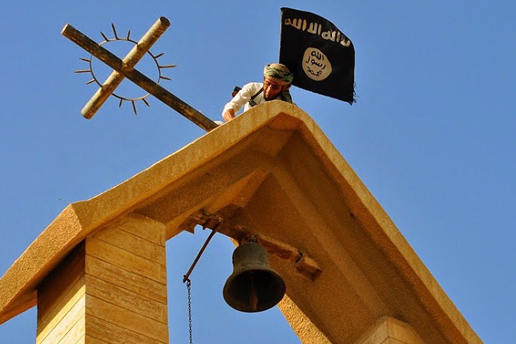 A member of Islamic State holds up its flag as he dismantles a cross on the top of a church in Mosul, Iraq, in this photo released by a militant website. Photo: AP