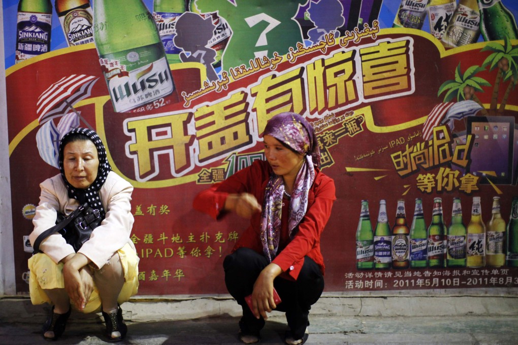 Uygur ethnic women sit in front of a beer advertisement near a market in Kashgar, Xinjiang province, in 2011. Photo: Reuters