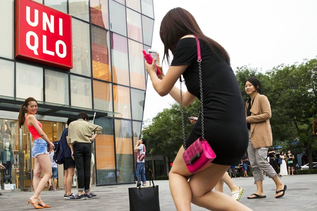 A Chinese woman poses for photo outside the Uniqlo flagship store where a steamy video purportedly taken inside one of its fitting rooms showing a couple apparently having sex in Beijing. Photo: AP