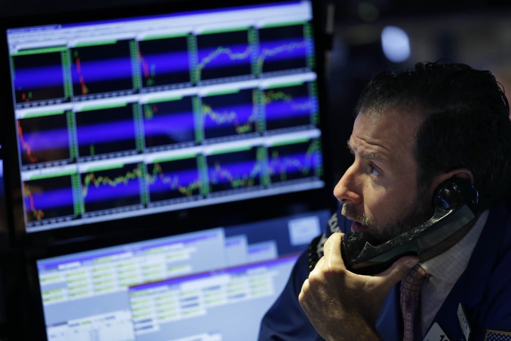 A trader on Wall Street works while the glow of electronic screens showing chart patterns of stock prices looms behind him. Photo: AP