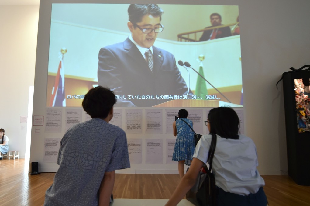Visitors look at a video work in which an artist plays the part of Japanese prime minister making a speech in poor English. Photo: AFP