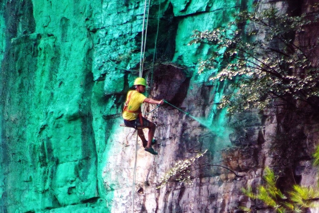 A worker dangles by a rope to spray-paint the cliff green. Photo: China Foto Press