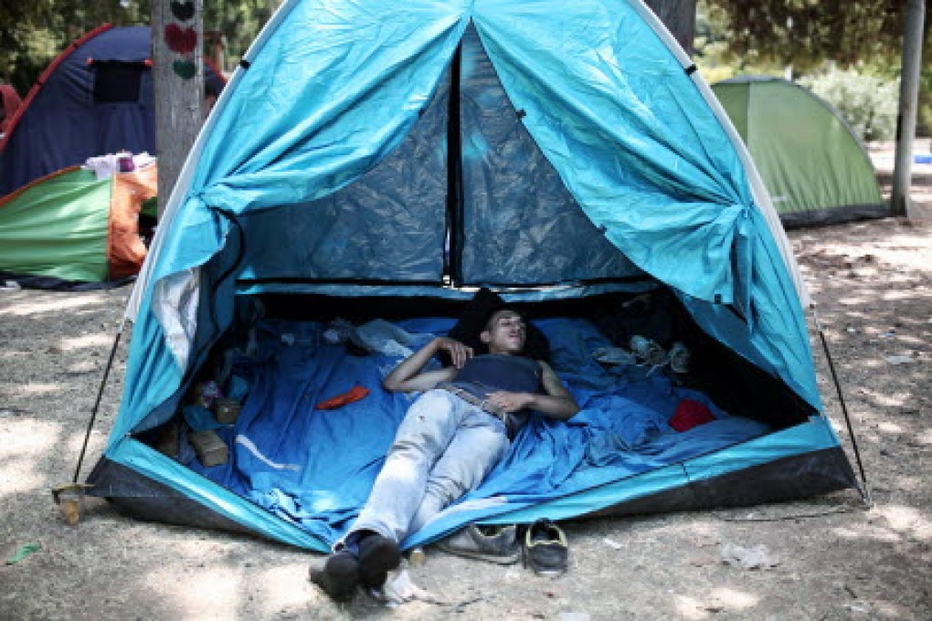 A migrant sleeps inside a tent in a park in central Athens. Photo: AFP