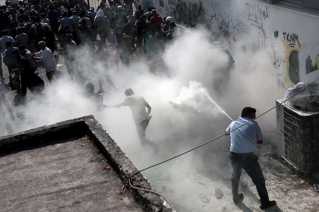 A policeman tries to disperse migrants with a fire extinguisher on Kos. Photo: AFP