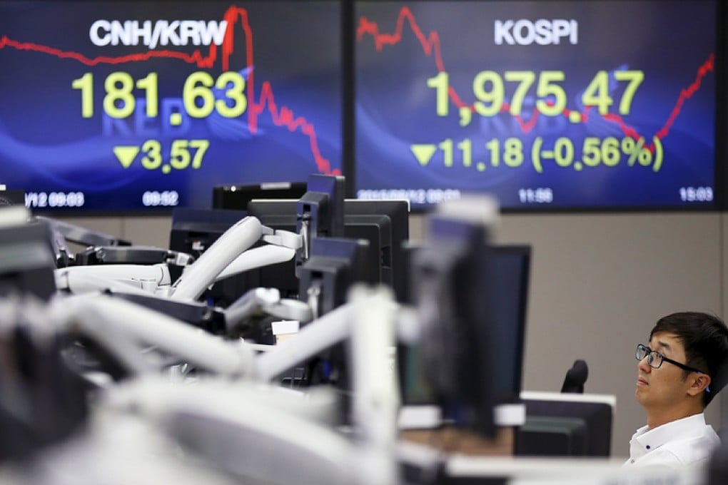 A currency dealer works in front of electronic boards showing the exchange rate between the Chinese yuan and South Korean won (left) and the Korea Composite Stock Price Index (KOSPI), at a dealing room of a bank in Seoul, South Korea, August 12, 2015. South Korea and other regional stock prices fell after China cut the value of its currency for the second day in a row. Photo: Reuters