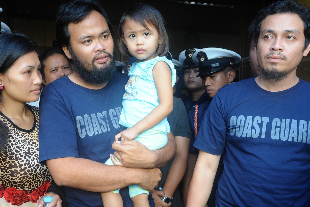 Philippine coastguards Rod Allain Pagaling (second left) carries his daughter Allian with wife Judith and his colleague Gringo Villaruz (right) are reunited with their families in Manila. Photo: AFP