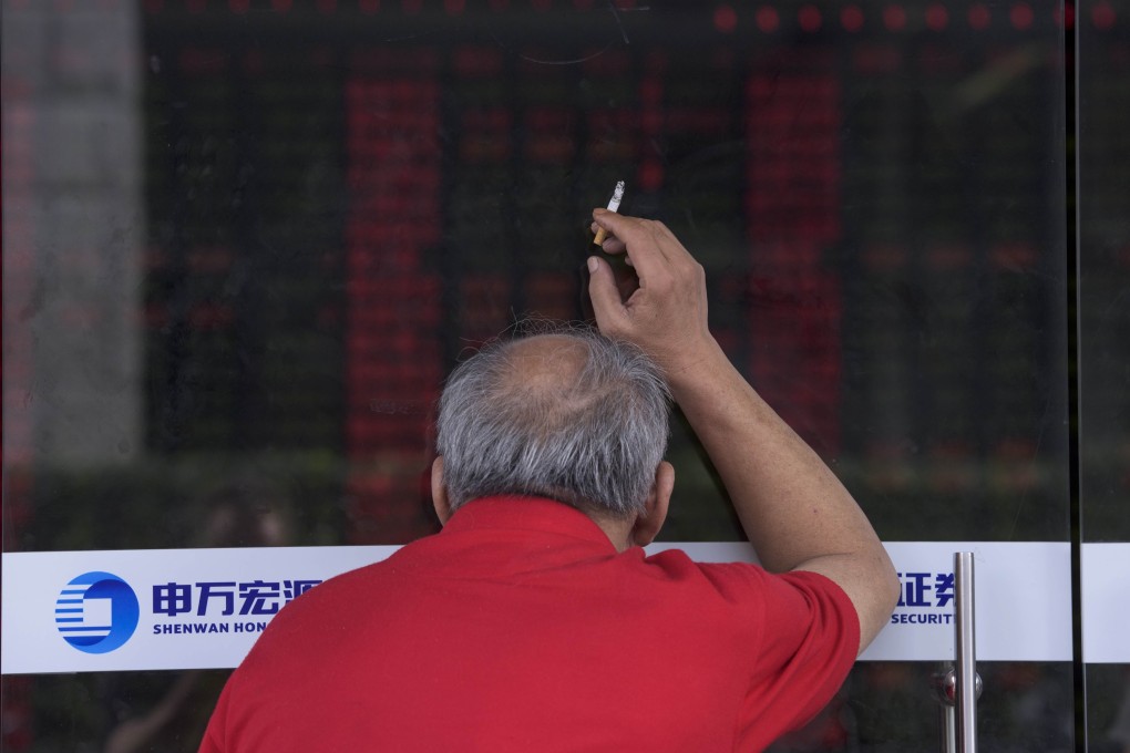 An investor holds a cigarette as he peers through a glass door to look at a digital board showing stock market movements at a brokerage house in Shanghai. Photo: AFP