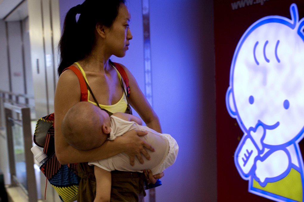 A woman carrying her baby walks by a cartoon logo at a shopping mall in Beijing, China. Photo: AP