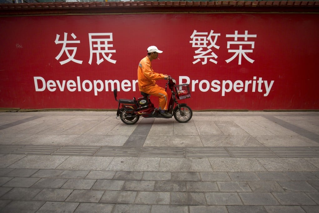 A maintenance worker rides a scooter past banners reading "Development" and "Prosperity" in English and Chinese on a street in central Beijing. Photo: AP
