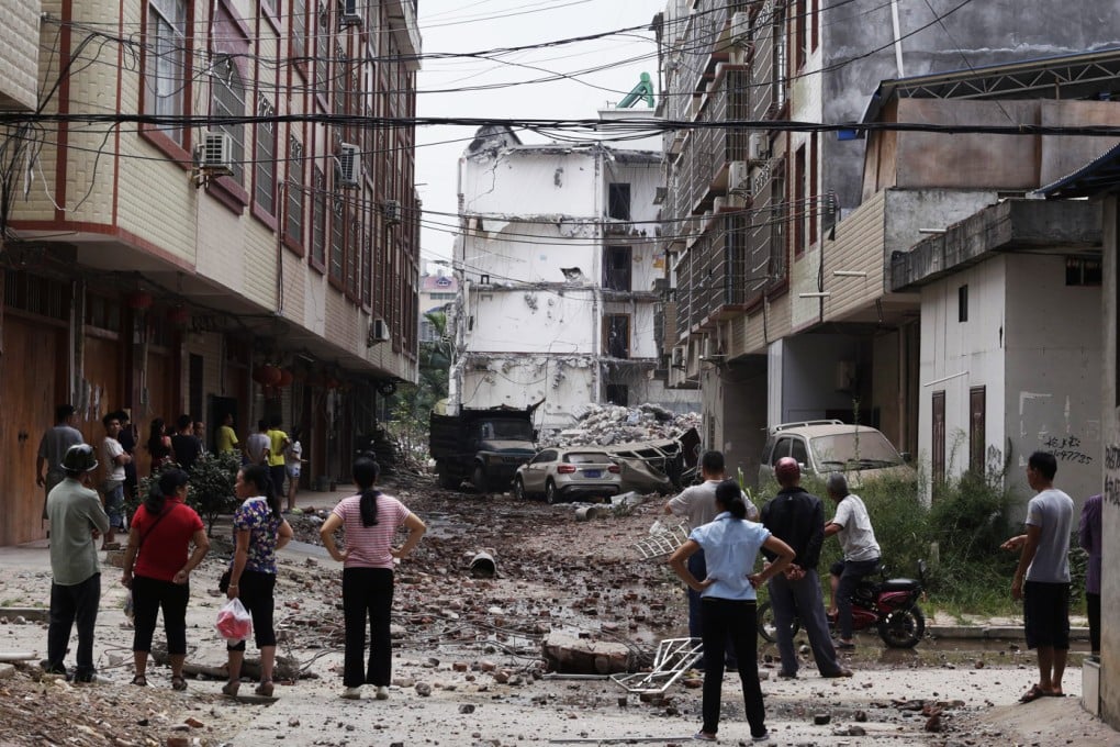 Local residents look at damaged vehicles and to the street near by a partially collapsed residential building after an explosion reportedly caused by explosives hidden in parcels. Photo: EPA