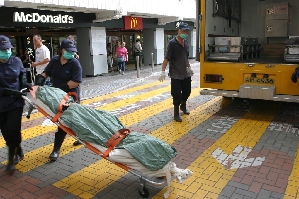 Workers remove the body of the homeless woman from the Ping Shek Estate McDonald's in Kowloon Bay on Sunday. Photo: SCMP Pictures