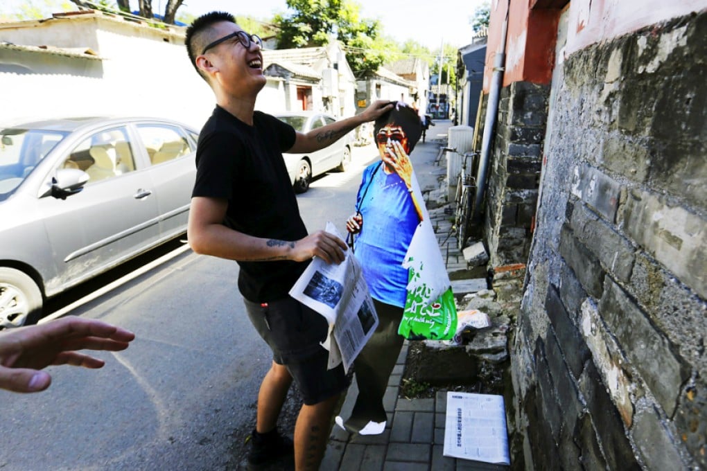 Chinese street artist 'ROBBBB' prepares to paste a life-sized image of a woman carrying her shopping to the door of an abandoned building in Beijing. Photo: Reuters