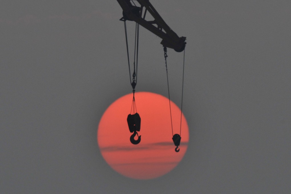 The hooks of a crane are pictured in front of the setting sun, at a port in Qingdao, Shandong province, China. Photo: Reuters