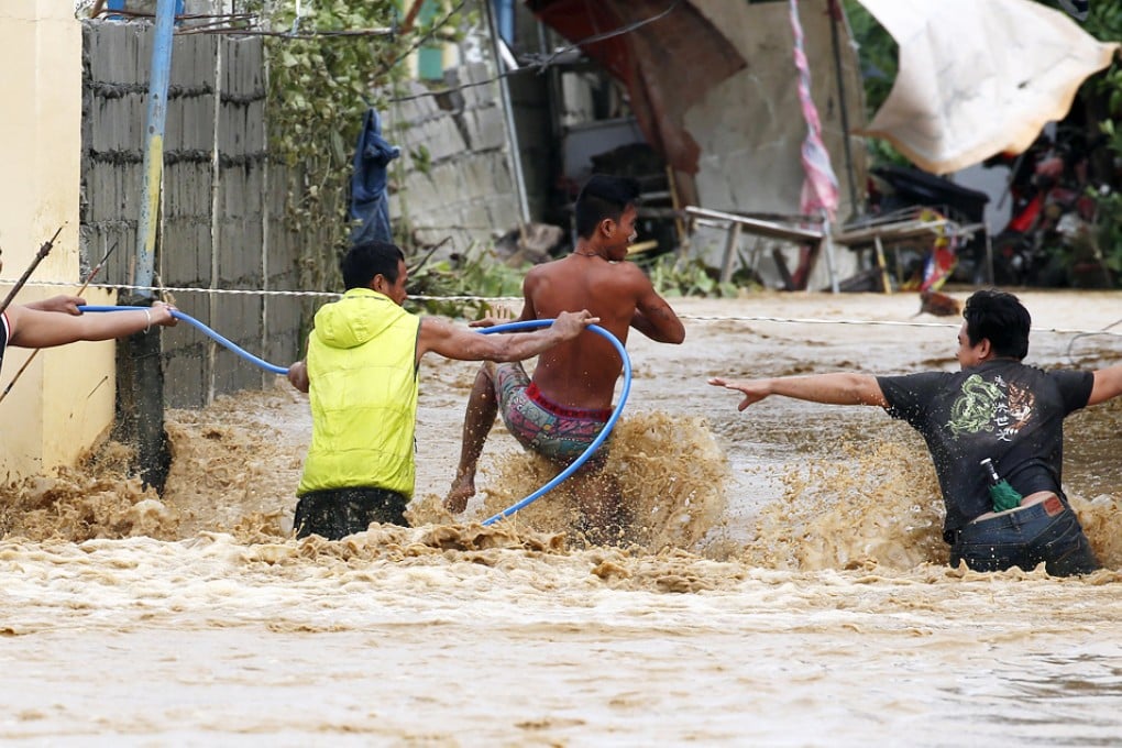 Residents use a plastic pipe and an electric wire to cross a flooded road amidst a strong current in Sta Rosa, Nueva Ecija, northern Philippines. Photo: Reuters