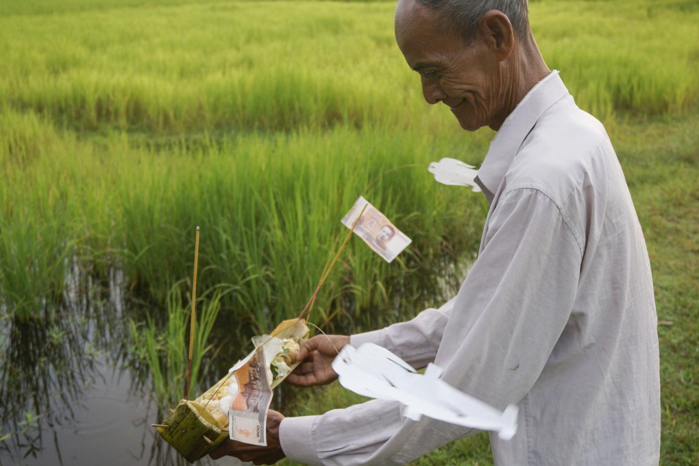 Farmer Supon's father-in-law releases paper ghosts and other offerings into his rice field in Baray village, Cambodia.