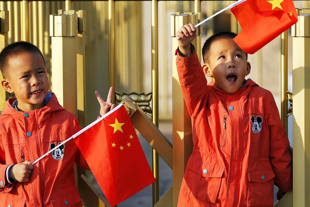 Chinese twin brothers Sun Qiyu and Sun Qichun wave national flags in Beijing on Monday. China must continue to enforce its one-child policy until new rules allowing all couples to have two children come into effect. Photo: Reuters