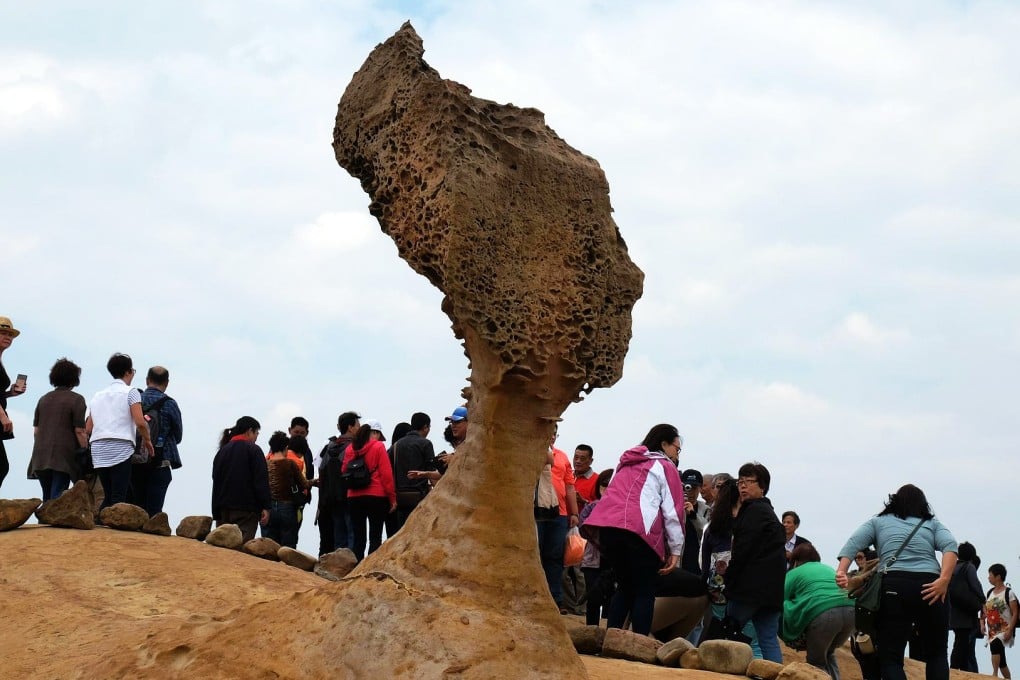 Tourists walk behind Taiwan's ancient "Queen's Head" rock in Yehliu, New Taipei City. The neck is getting thinner, experts say. Photo: AFP