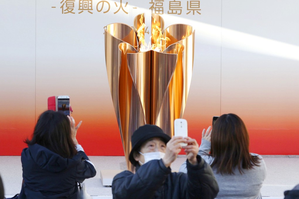 People wearing masks take pictures of the Olympic flame exhibited in Fukushima on March 24, 2020, before the Tokyo 2020 Olympic Games were postponed for a year. Photo: Kyodo