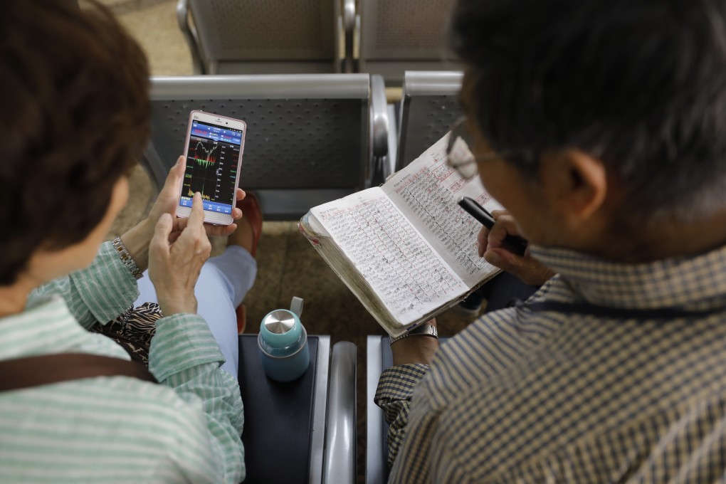 A Chinese investor checks stock prices in his notebook while another views them on her mobile phone in Beijing. Photo: EPA-EFE