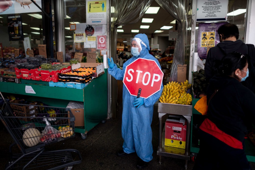 A worker wearing full-body protective gear holds a “Stop” sign in front of a food market as he manages the flow of the customers on May 18, 2020 in the Jackson Heights neighbourhood of New York City. Photo: AFP