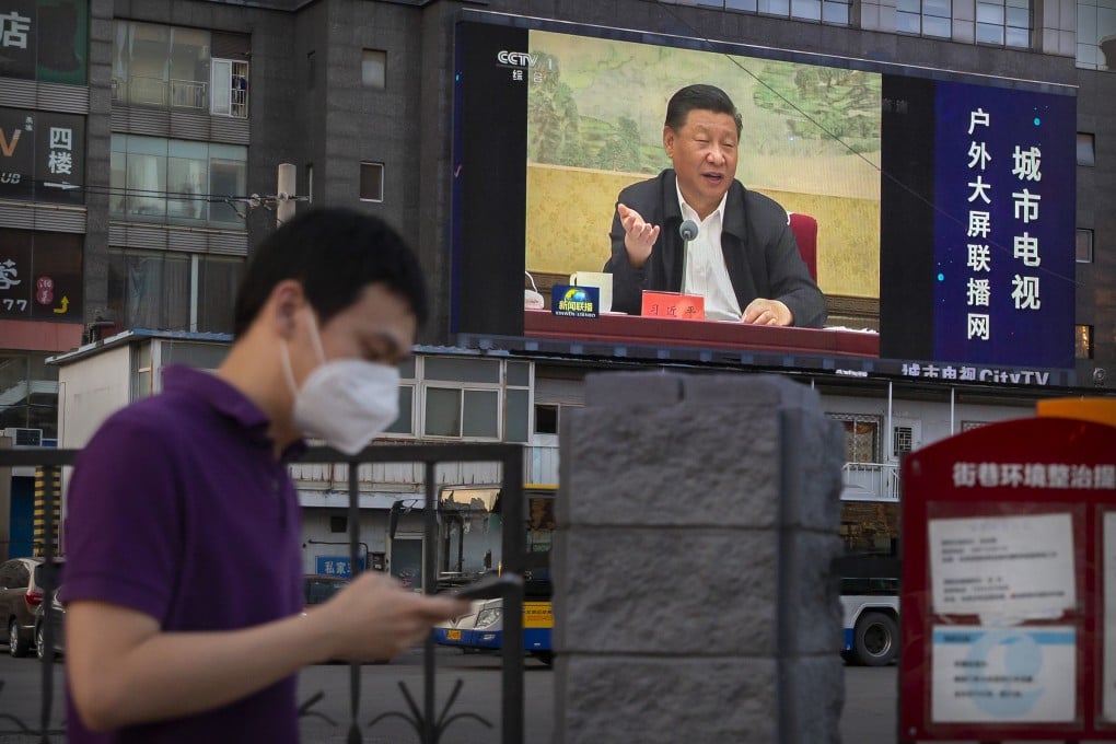A man looks at his phone while walking past
a giant screen in Beijing showing Chinese President Xi Jinping. In China, internet code words referring to Xi are banned on social media. Photo: AP