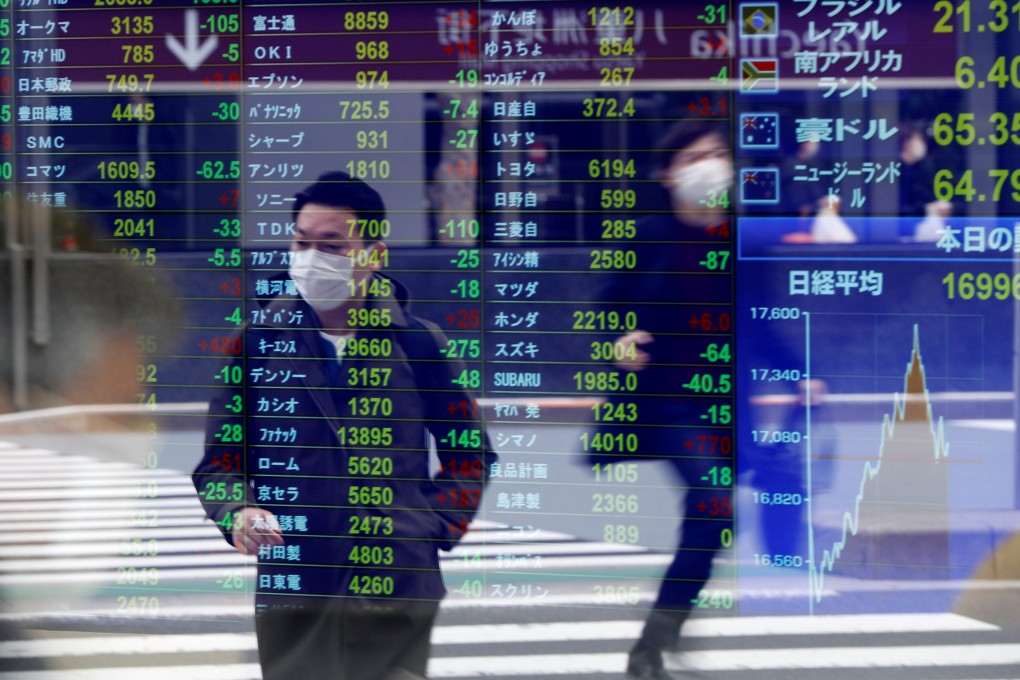 Passersby wearing protective face masks are reflected on a screen displaying stock prices outside a brokerage in Tokyo in March 2002. Photo: Reuters