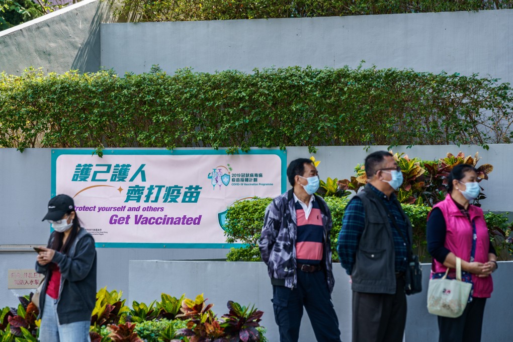 People wait in front of a banner promoting the Covid-19 inoculation programme outside a community vaccination centre in Hong Kong. Photo: Bloomberg