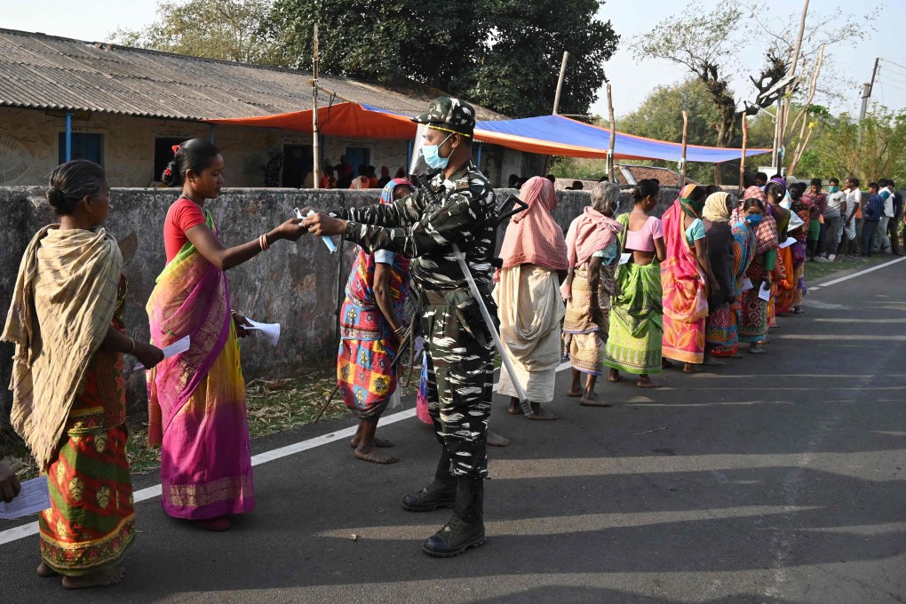 A paramilitary personnel distributes facemasks to voters standing in queue to cast their ballots in West Bengal. Photo: AFP