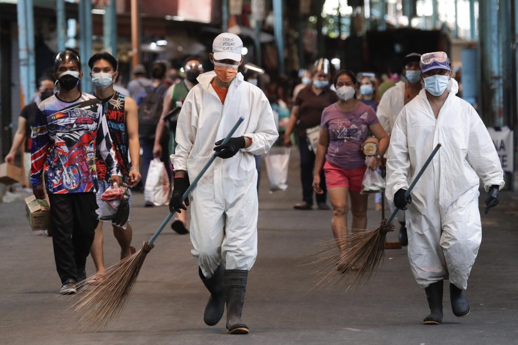 Workers wearing protective suits walks beside residents at a public market during the start of a stricter lockdown in Manila. Photo: AP
