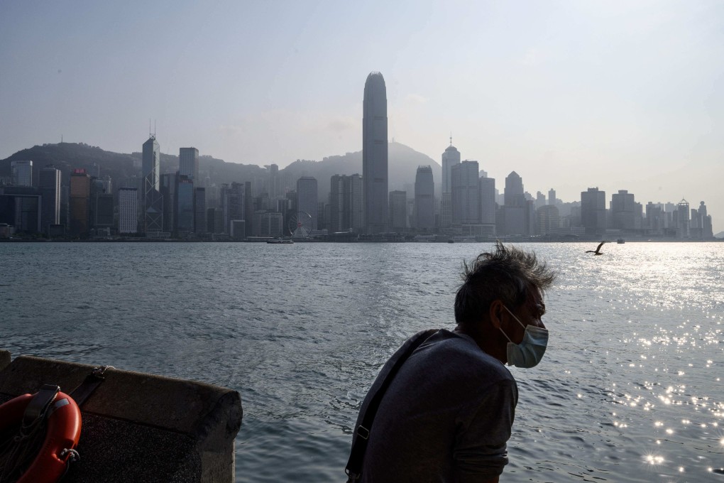 A man relaxes on a Kowloon promenade that runs along Victoria Harbour, with the skyline of Hong Kong Island in the background on March 18, 2021. (Photo by Anthony WALLACE / AFP)