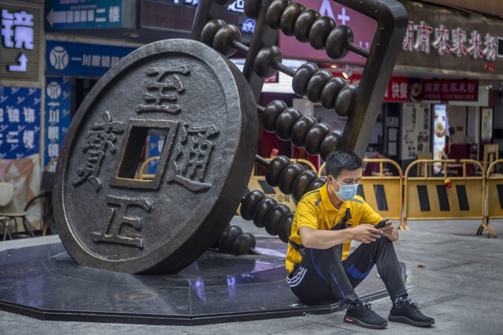 A man sits next to a sculpture of a Chinese coin and abacus in Guangzhou, China, on May 14, 2020. Photo: EPA-EFE