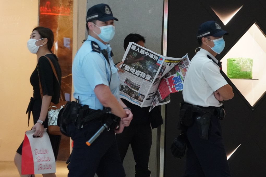 An Apple Daily reader browses a copy of the final edition of the newspaper as police officers walk by in Central, on June 24. Photo: Felix Wong