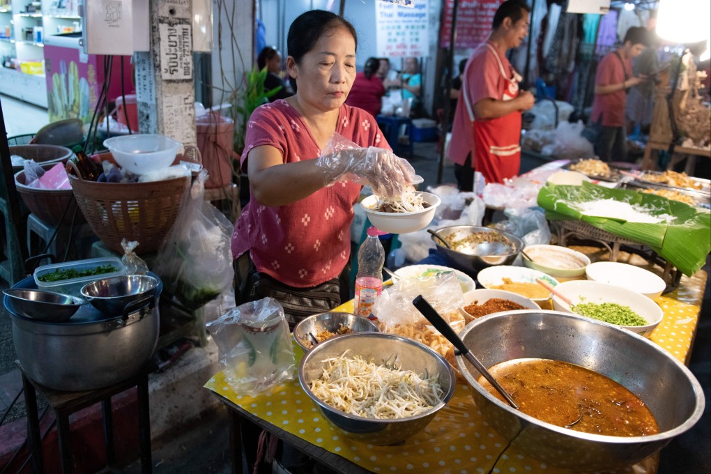 A woman sells street food at a night market in Chiang Mai, Thailand. The origins of the kingdom’s best culinary dishes is examined in cookbook The Food of Thailand. Photo: Getty Images
