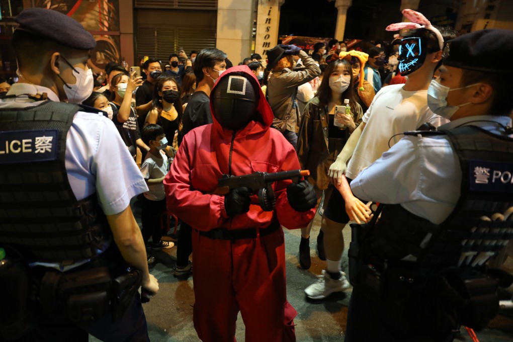 Halloween party-goers, one wearing a Squid Game square mask, stand next to police officers at Lan Kwai Fong in Central on October 31. Photo: Xiaomei Chen