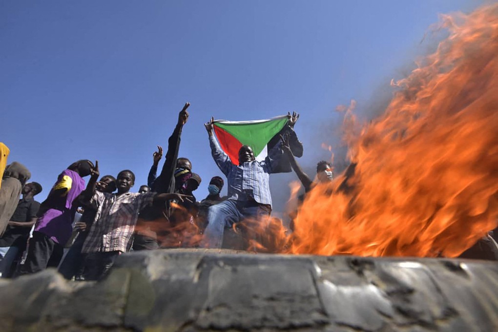 A man holds a Sudanese flag before flames at a barricade as people protest against the military coup in “Street 60” in the capital of Khartoum on November 13. Photo: AFP