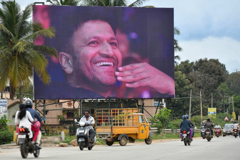 Commuters drive past a poster of late Indian film star Puneeth Rajkumar Bangalore. Photo: AFP