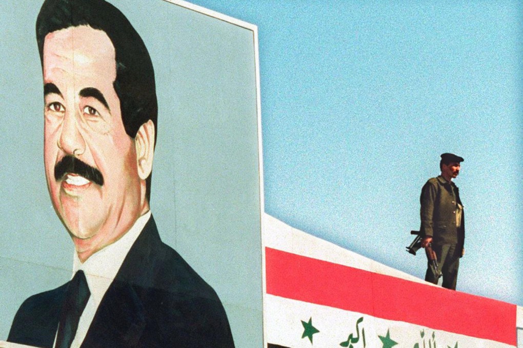 A soldier stands guard on top of a building draped with the Iraqi flag next to a portrait of President Saddam Hussein in Iraq in November 1997. Photo: AFP