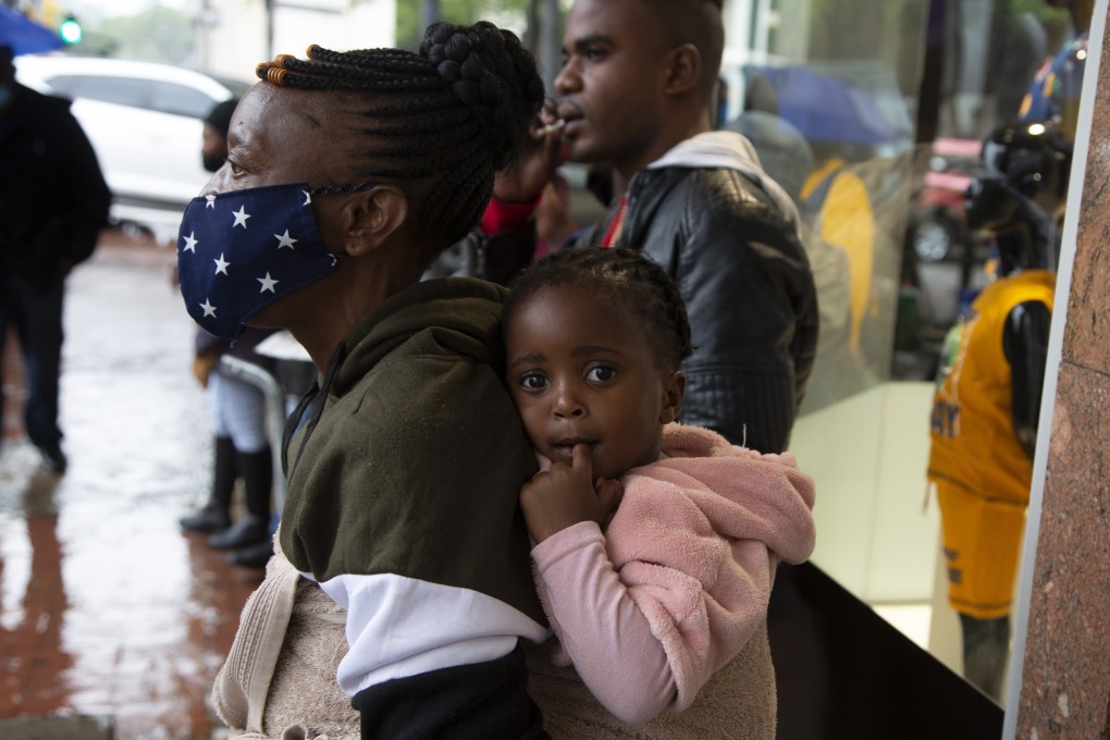 A woman wearing a face mask holds a child on her back on a crowded street in Pretoria, South Africa, on November 27. Photo: AP
